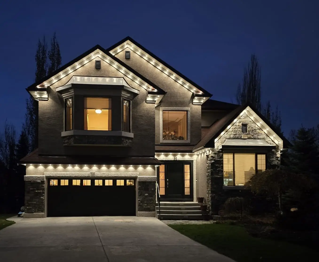 Govee permanent lights mounted under the eaves of a two-storey home, shining down onto the walls in warm white at blue hour