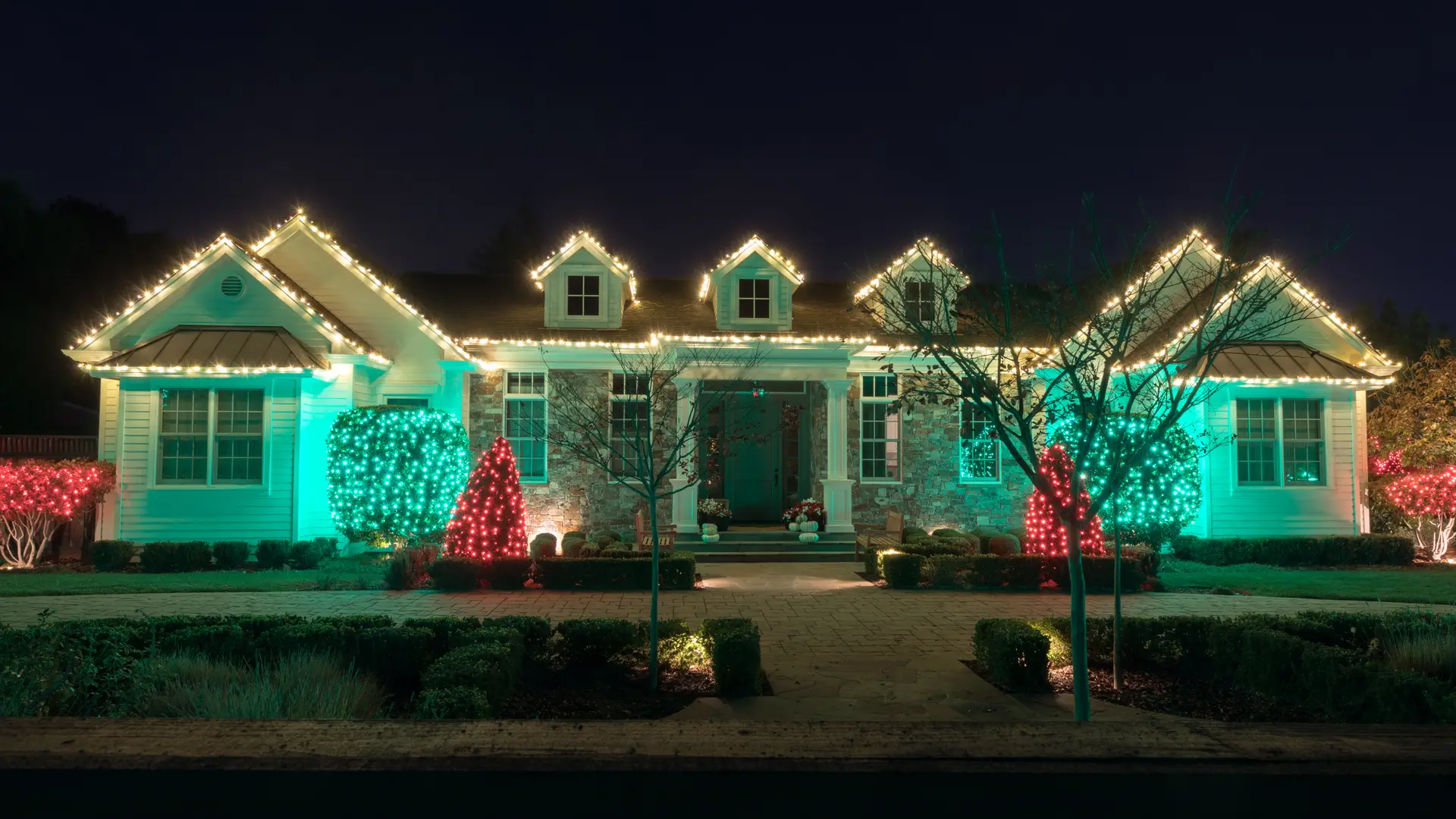 Bungalow lit in multicolour Christmas lights with red and green wrapped shrubs