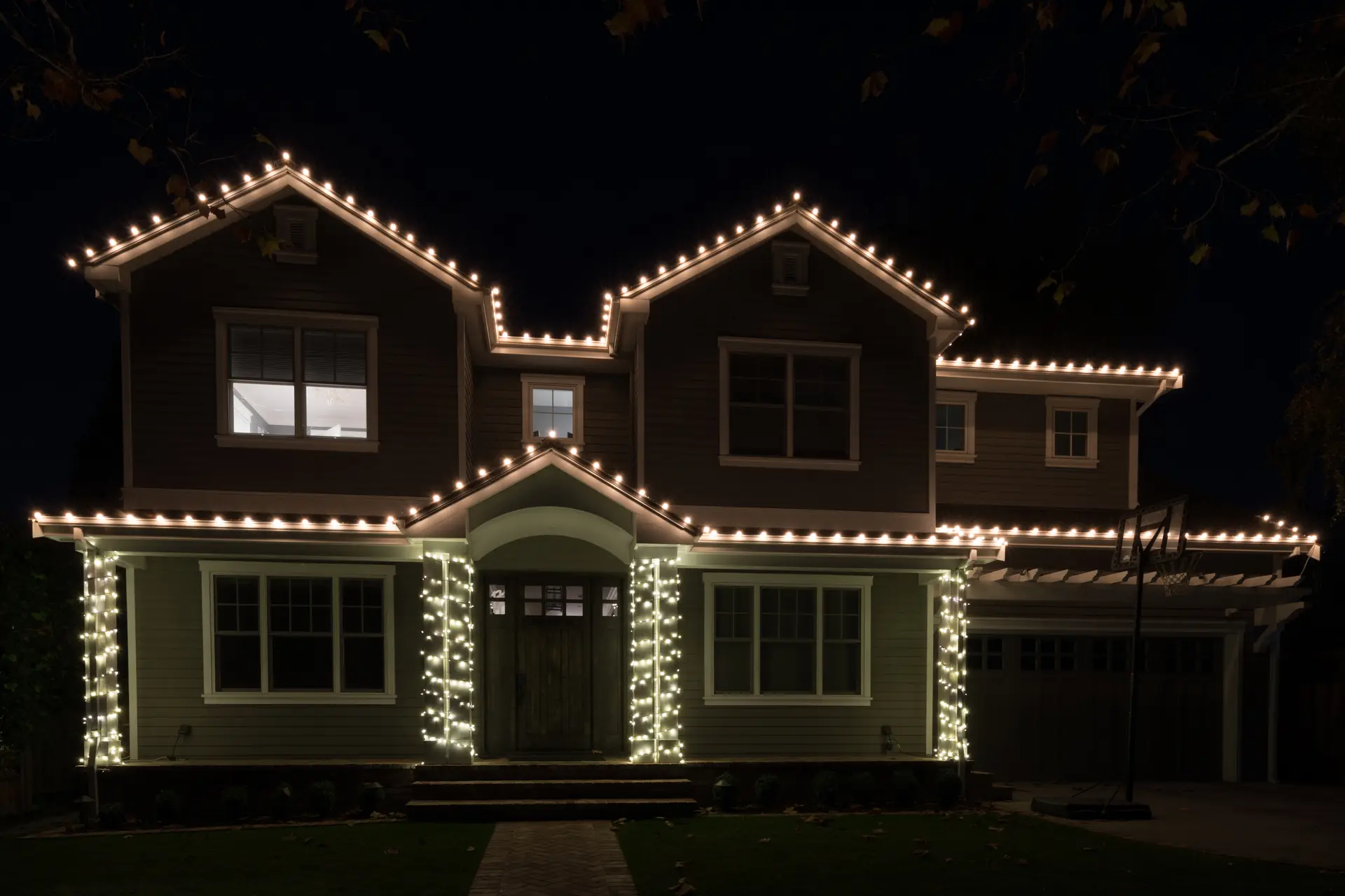 Two-storey home with warm white lights on the roofline and wrapped porch pillars