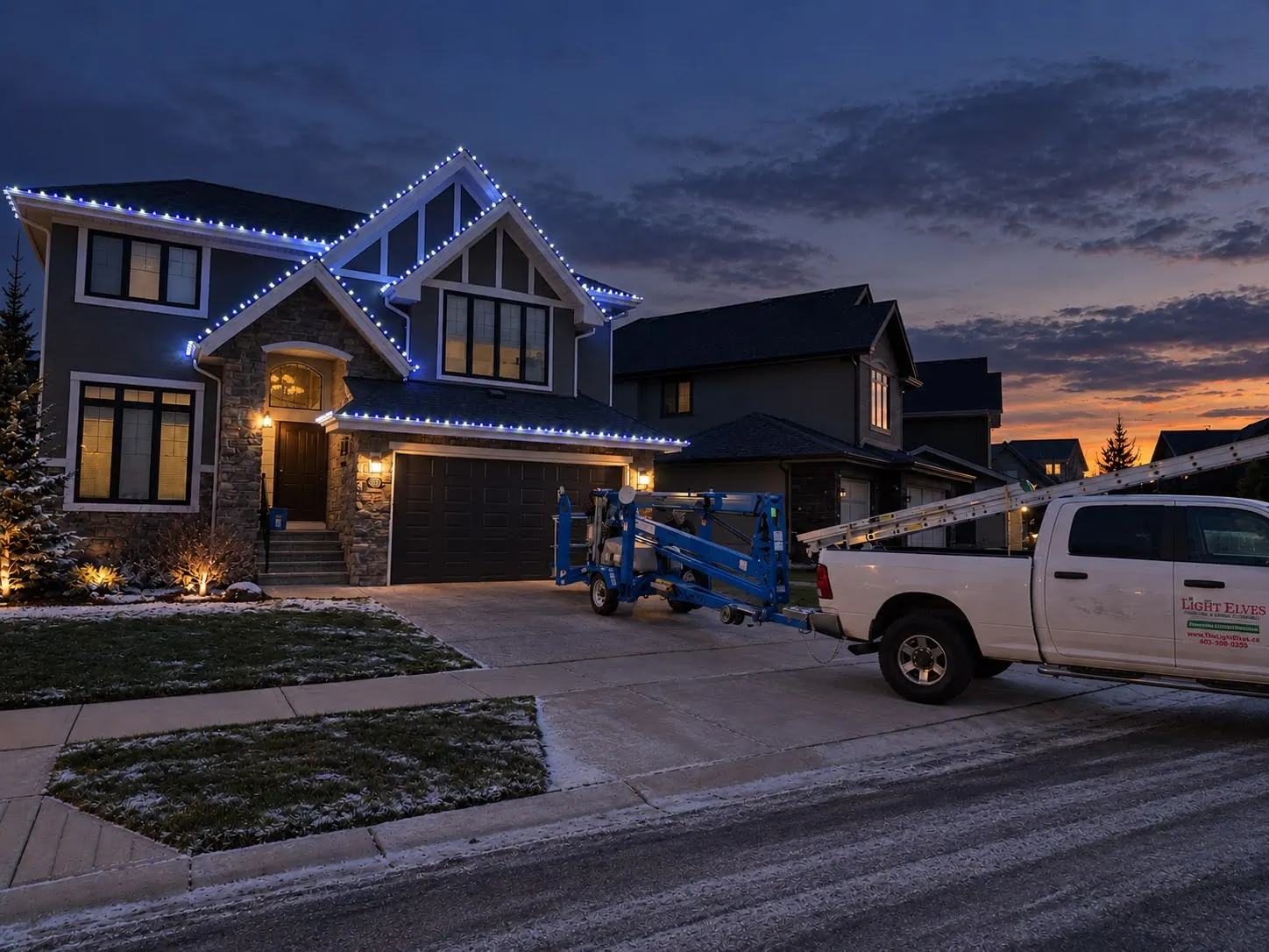 Two-storey home with cool white lights along every gable, with the Light Elves truck and lift in the driveway at dusk