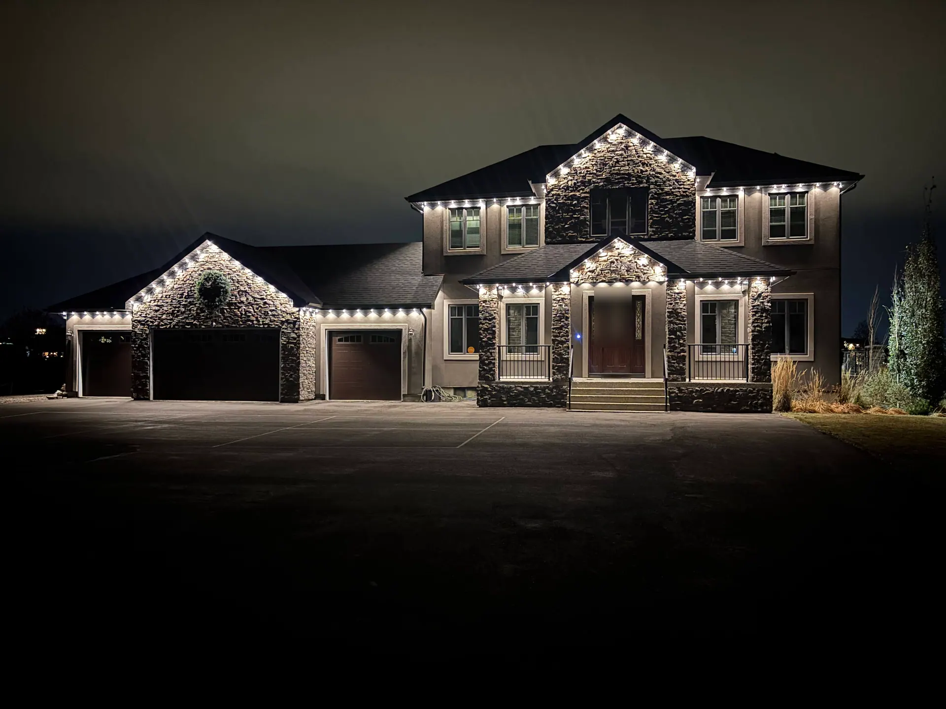 Govee lights mounted under every eave of a two-storey stone-front home, shining down in warm white at night